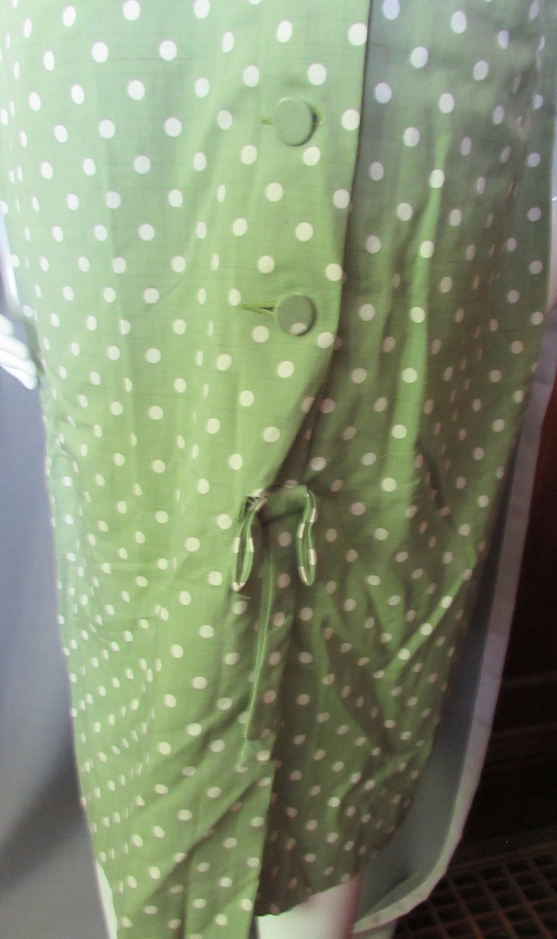 May include: A green dress with white polka dots and a tie at the waist. The dress has three buttons on the front.