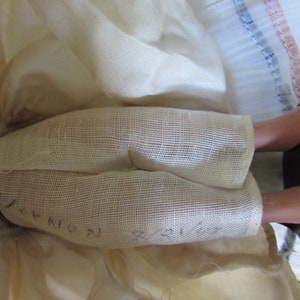 May include: Close-up of a doll's legs wearing white fabric pants with a mesh texture. The fabric has the words "Queen" and "Princess" written on it. The doll's legs are made of porcelain and are wearing black shoes.
