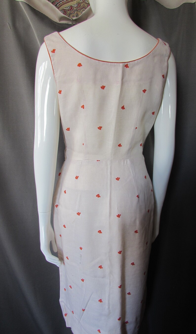 May include: A sleeveless white dress with a scoop neck and a small orange floral pattern.