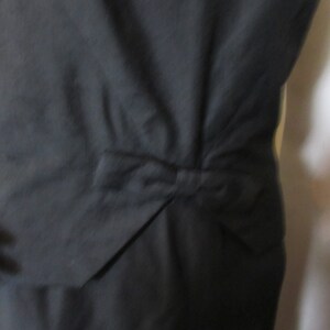 Puede incluir: Un vestido negro con un detalle de lazo en la espalda.