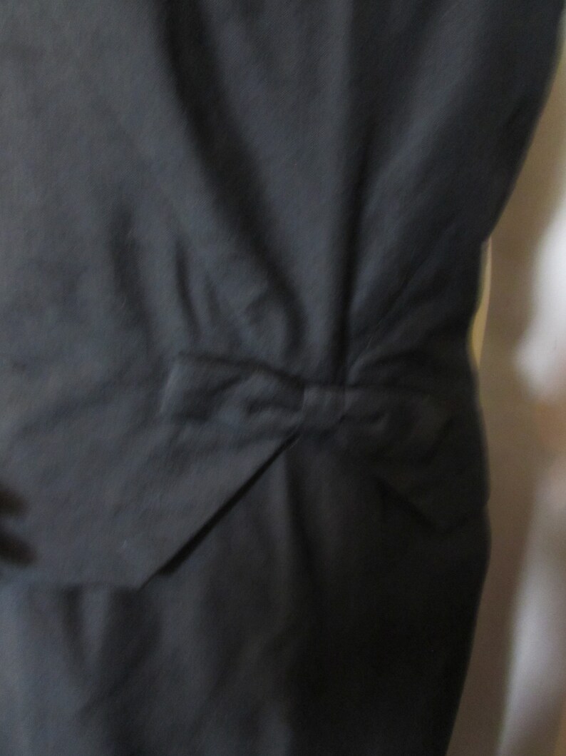 Puede incluir: Un vestido negro con un detalle de lazo en la espalda.