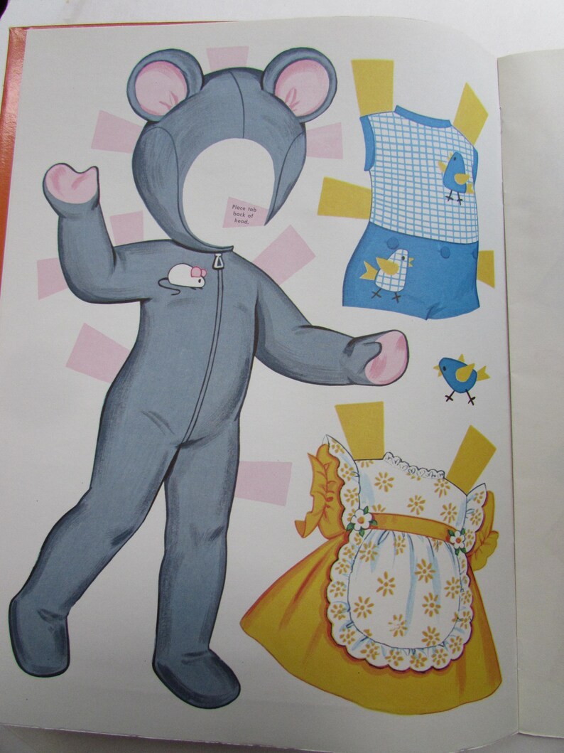 May include: A vintage paper doll set featuring a gray mouse costume with pink accents, a blue and white checkered outfit with bird graphics, and a yellow dress with a white floral apron. The set is open on a white background.