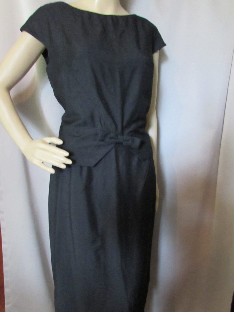 Puede incluir: Un vestido negro sin mangas con un lazo en la cintura.