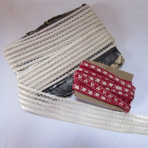 May include: Two spools of trim, one white and one red. The white trim is a delicate lace with a woven pattern. The red trim has a repeating pattern of white dots and a stylized flower design.