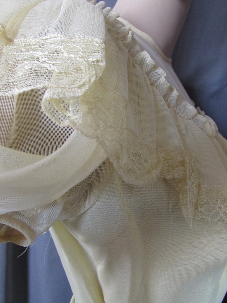 May include: A white sheer top with a lace trim around the neckline and sleeves. The top is made of a lightweight fabric and has a delicate, feminine look.