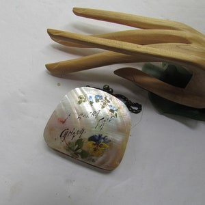 May include: A small, white, iridescent, shell purse with a silver chain. The purse is decorated with hand-painted flowers and the words "I never forget" in cursive.