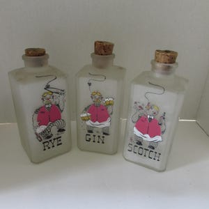 Puede incluir: Tres botellas de vidrio esmerilado con tapones de corcho, cada una con una ilustración de dibujos animados de un hombre con un chaleco rosa. Las botellas están etiquetadas como "RYE", "GIN" y "SCOTCH".