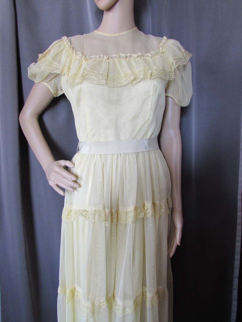 May include: A pale yellow vintage dress with a lace trim and a sheer overlay. The dress has a fitted bodice and a flowing skirt.