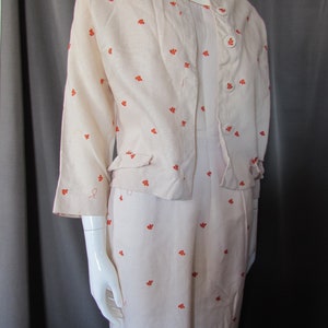 May include: A white linen dress with a matching jacket, both featuring a small orange floral pattern. The dress has a button-up front and the jacket has a button-up closure.
