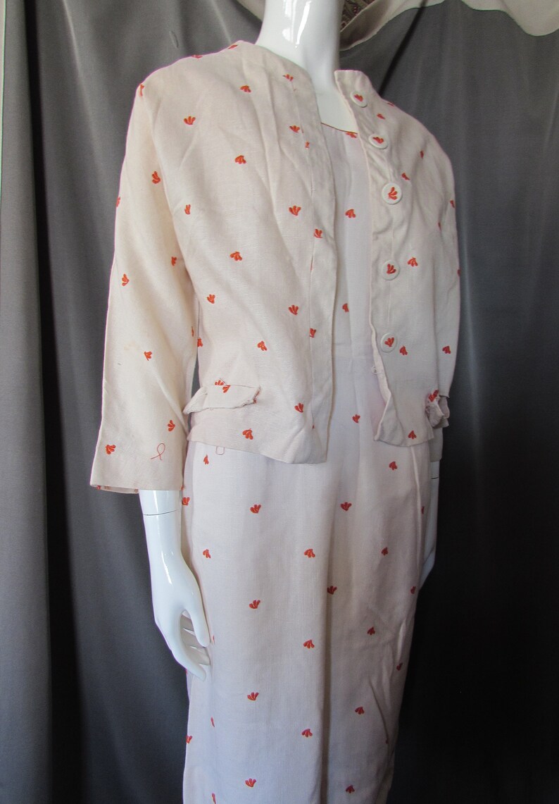 May include: A white linen dress with a matching jacket, both featuring a small orange floral pattern. The dress has a button-up front and the jacket has a button-up closure.