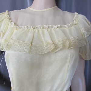 May include: A pale yellow sheer blouse with a ruffled neckline and lace trim. The blouse has short sleeves and a fitted bodice.