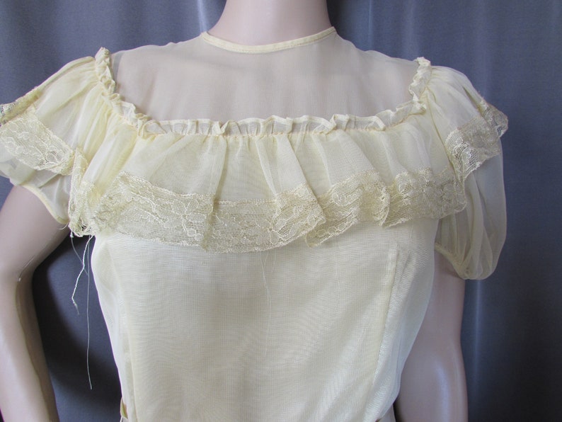 May include: A pale yellow sheer blouse with a ruffled neckline and lace trim. The blouse has short sleeves and a fitted bodice.