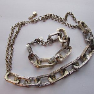 May include: A silver and gold chain necklace and bracelet set with textured links. The necklace is longer than the bracelet.