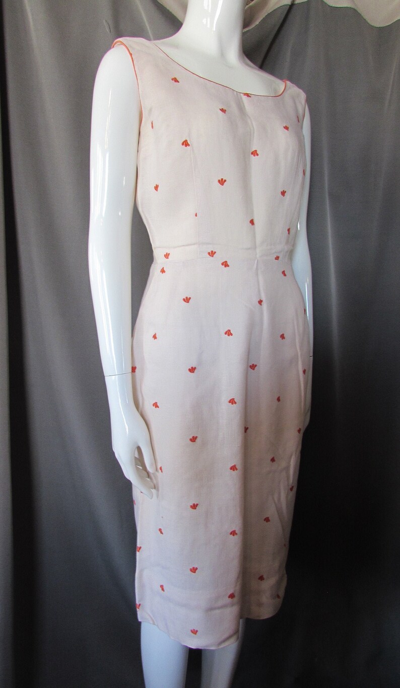 May include: A sleeveless white dress with a scoop neck and a small floral pattern in orange. The dress is fitted and has a straight skirt.