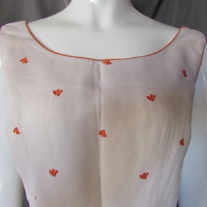 May include: A sleeveless white linen dress with a scoop neck and orange embroidered floral details.