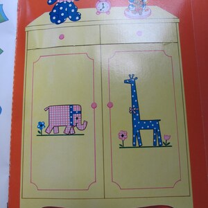 May include: A children's book illustration featuring a yellow wardrobe with pink trim and cartoon animal designs. A blue polka-dotted dog, a pink clock, and a lamp are on top. The wardrobe doors depict a pink elephant and a blue giraffe.