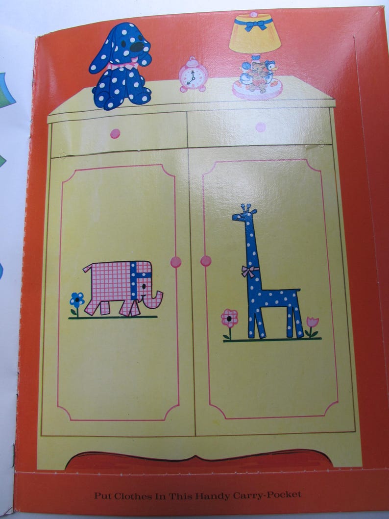 May include: A children's book illustration featuring a yellow wardrobe with pink trim and cartoon animal designs. A blue polka-dotted dog, a pink clock, and a lamp are on top. The wardrobe doors depict a pink elephant and a blue giraffe.