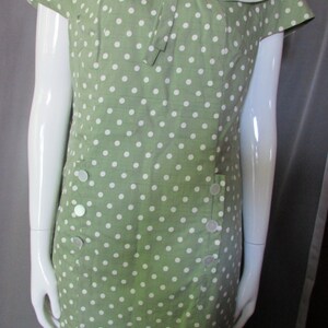 May include: A green polka dot dress with a white collar and bow. The dress has short sleeves and a fitted silhouette.