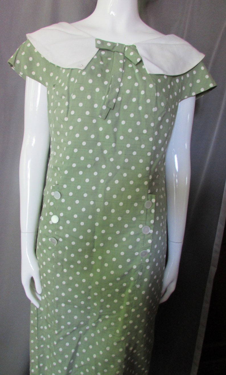 May include: A green polka dot dress with a white collar and bow. The dress has short sleeves and a fitted silhouette.