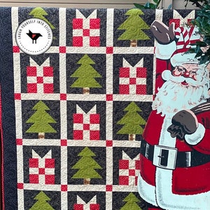 May include: A black and white quilt with a red and white checkered pattern and green trees. The quilt is hanging on a wall with a Santa Claus cutout in front of it. The quilt has the text "Laugh Yourself Into Stitches" in a black circle.