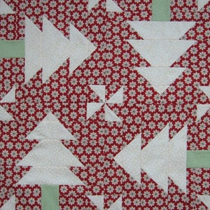 May include: A close-up of a quilt with a repeating pattern of white Christmas trees and pinwheels on a red background with small white and gray floral designs. The trees have green rectangular bases.