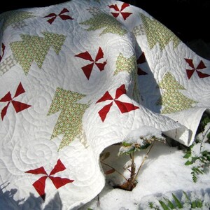 May include: A white quilt with a Christmas tree and pinwheel design. The quilt features green Christmas trees with red and white accents. The quilt is made of soft fabric and is suitable for a bed or sofa.