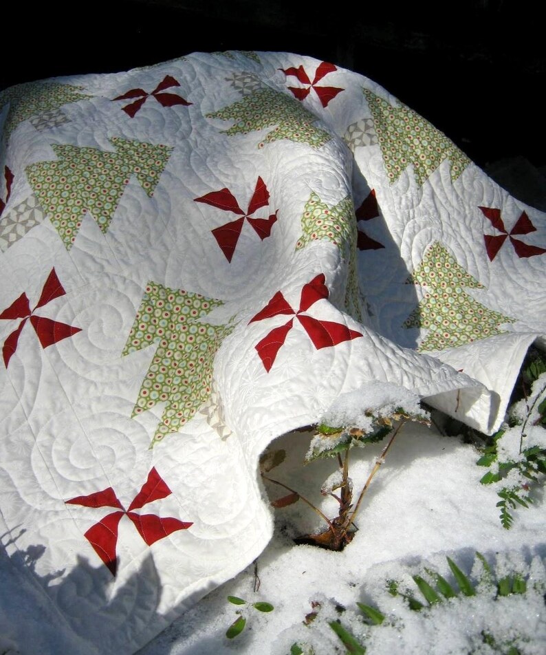 May include: A white quilt with a Christmas tree and pinwheel design. The quilt features green Christmas trees with red and white accents. The quilt is made of soft fabric and is suitable for a bed or sofa.