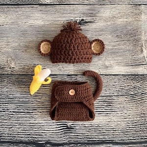 May include: A brown crocheted monkey costume for a baby, including a hat with ears, a diaper cover, and a banana prop.