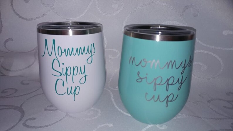 May include: Two stainless steel tumblers with a white and teal blue finish. The tumblers have the text "Mommy's Sippy Cup" written on them in a teal blue color.