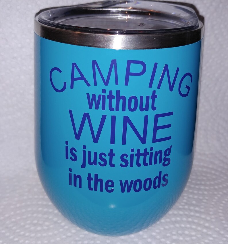 May include: A turquoise stainless steel tumbler with a silver lid. The tumbler has the text "Camping without wine is just sitting in the woods" printed in blue.