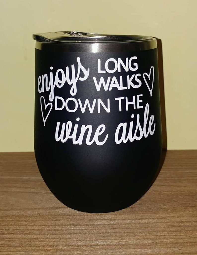 May include: Black stainless steel wine tumbler with a white graphic that reads "enjoys long walks down the wine aisle" with a heart symbol on either side of the text.