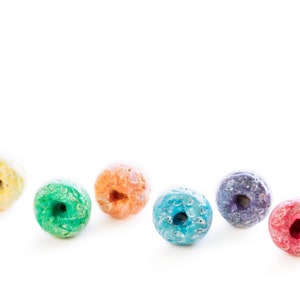May include: A row of six colourful cereal rings, each a different colour of the rainbow, arranged in a line on a white background.