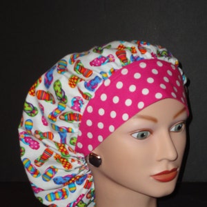 May include: A white scrub hat with a pink and white polka dot trim. The hat has a colorful print of flip flops on it.