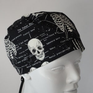 May include: Black and white skull and skeleton print scrub hat with the text "The Human Bodies" and anatomical labels.