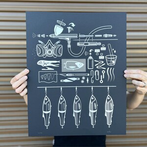May include: A black and white illustration of a fishing lure painting process. The illustration includes a respirator mask, airbrush, paint, and other tools. There are five fishing lures hanging from a line at the bottom of the illustration.
