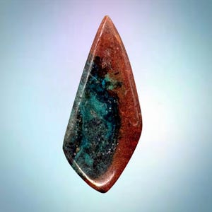 May include: A polished, teardrop-shaped gemstone cabochon featuring a striking blend of deep rust-red, earthy brown, and vibrant turquoise-blue mineral inclusions. The surface is smooth and glossy, showcasing a natural, irregular colour pattern.
