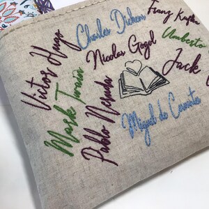 May include: Beige linen tote bag embroidered with the names of famous authors in various colors. The names include Victor Hugo, Mark Twain, and Charles Dickens. A small embroidered book with a heart is also featured.