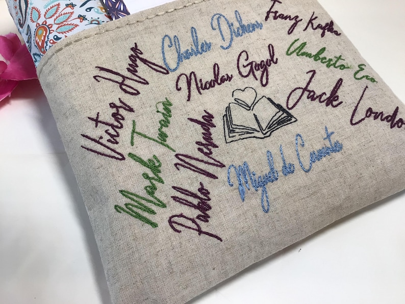 May include: Beige linen tote bag embroidered with the names of famous authors in various colors. The names include Victor Hugo, Mark Twain, and Charles Dickens. A small embroidered book with a heart is also featured.