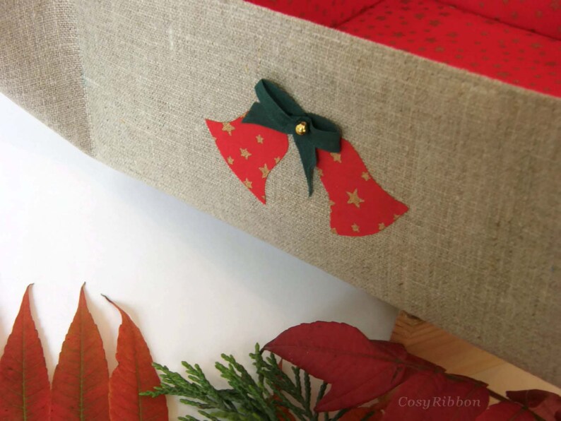May include: A linen storage box with a red and gold star pattern and a green bow with a gold bell. The box is decorated with two red bells with gold stars.