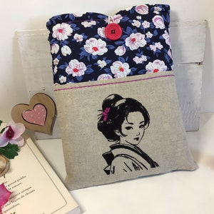 K&ouml;nnte beinhalten: Eine Buchh&uuml;lle mit einem Blumendruck auf der Vorderseite und einem gestickten Schwarzwei&szlig;bild einer Frau mit einer Blume im Haar auf der R&uuml;ckseite. Die H&uuml;lle hat einen rosa Knopfverschluss.