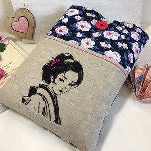 K&ouml;nnte beinhalten: Eine Tasche aus Leinen und Blumenstoff mit einem gestickten Schwarzwei&szlig;bild einer Frau mit einer Blume im Haar. Die Tasche hat einen roten Knopfverschluss.