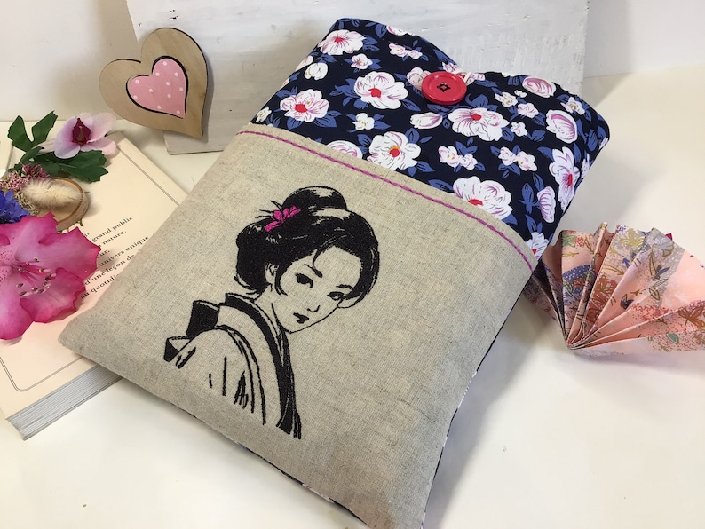 K&ouml;nnte beinhalten: Eine Tasche aus Leinen und Blumenstoff mit einem gestickten Schwarzwei&szlig;bild einer Frau mit einer Blume im Haar. Die Tasche hat einen roten Knopfverschluss.