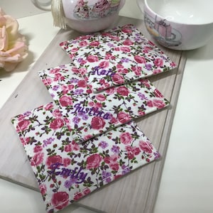 Peut inclure: Trois dessous-de-verre en tissu floral avec des noms personnalisés : "Katie", "Justina" et "Emily".