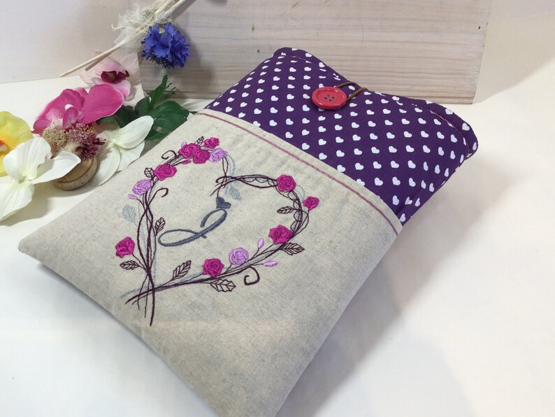 Może przedstawiać: Beżowa torebka z lnu z fioletową kieszenią z białymi sercami. Torebka ma haftowany wz&oacute;r kwiatowy w kształcie serca z literą "B" w środku. Czerwony guzik jest przymocowany do g&oacute;rnej części torebki.