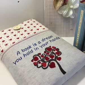 Puede incluir: Una cubierta de libro gris y blanca con un dise&ntilde;o de &aacute;rbol de corazones rojos y el texto "Un libro es un sue&ntilde;o que tienes en tus manos".