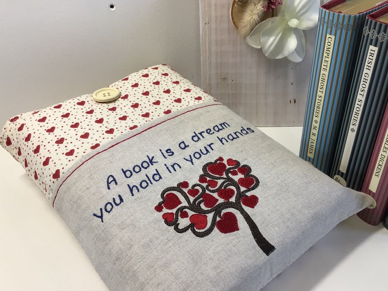 Puede incluir: Una cubierta de libro gris y blanca con un dise&ntilde;o de &aacute;rbol de corazones rojos y el texto "Un libro es un sue&ntilde;o que tienes en tus manos".