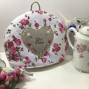 Peut inclure: Une housse de thé blanche avec un motif de roses roses et un cœur brun brodé avec le texte "Tea Time".