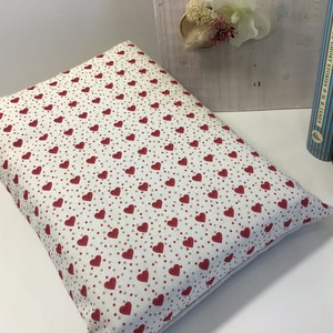 Puede incluir: Una almohada blanca con un patr&oacute;n de corazones rojos y peque&ntilde;os puntos rojos. La almohada es rectangular y tiene una textura suave y mullida.