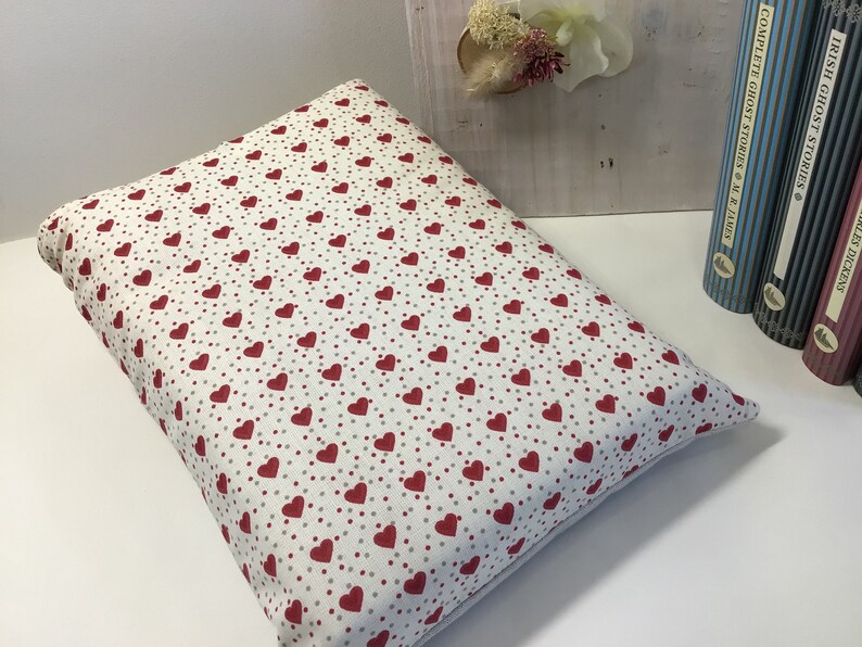 Puede incluir: Una almohada blanca con un patr&oacute;n de corazones rojos y peque&ntilde;os puntos rojos. La almohada es rectangular y tiene una textura suave y mullida.