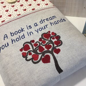 Puede incluir: Una funda de libro gris con corazones rojos y el texto "Un libro es un sue&ntilde;o que tienes en tus manos".